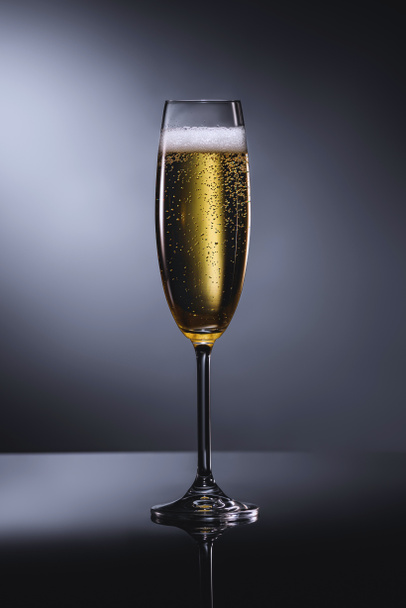close up view of glass of champagne with foam on dark backdrop - Fotoğraf, Görsel