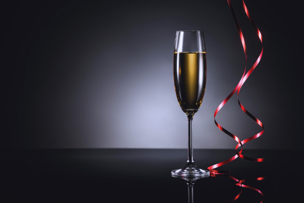 close up view of glass of champagne and festive confetti on dark backdrop - Фото, изображение