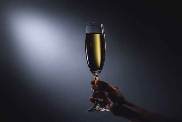 partial view of woman holding glass of champagne in hand on dark backdrop - Φωτογραφία, εικόνα