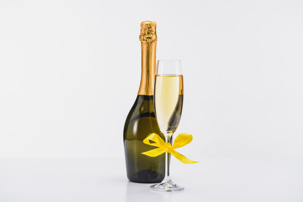 Nahaufnahme von Flasche und Glas Champagner mit gelbem Band auf weißem Hintergrund  - Foto, Bild