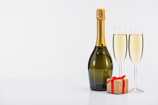 close up view of bottle and glasses of champagne with wrapped gift on white background - Foto, afbeelding