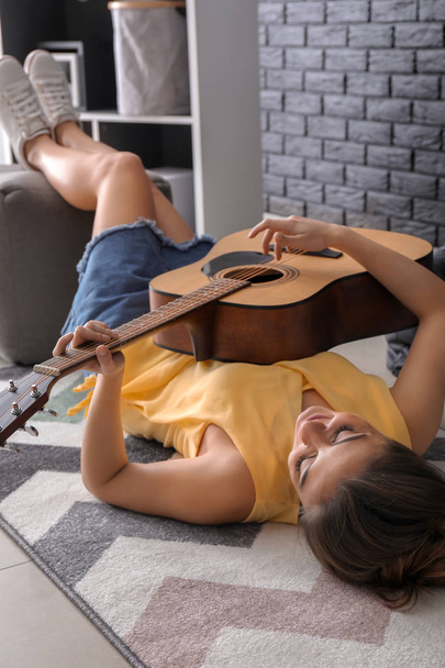 Beautiful woman playing guitar while lying on floor - Foto, Bild