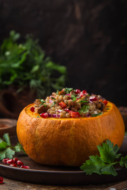 whole pumpkin stuffed with barley and vegetables, served with pomegranate and parsley, rustic background, selective focus - Photo, image