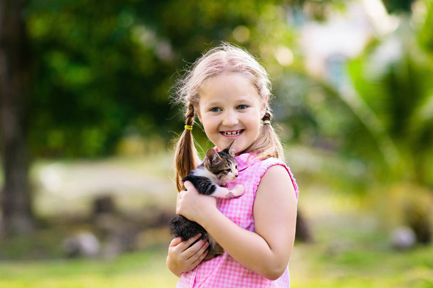 Παιδί που κρατάει τη γάτα. Παιδιά και κατοικίδια. Κοριτσάκι αγκαλιάζει χαριτωμένο μικρό γατάκι στον καλοκαιρινό κήπο. Οικογενειακό ζώο με παιδιά. Παιδιά με κατοικίδια ζώα συντροφιάς.  - Φωτογραφία, εικόνα