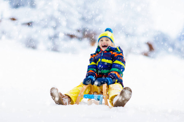 Kleine jongen geniet van een slee ritje. Kindersleeën. Een peuter op een slee. Kinderen spelen buiten in de sneeuw. Kinderen slee in de Alpen bergen in de winter. Outdoor plezier voor familie Kerstvakantie. - Foto, afbeelding