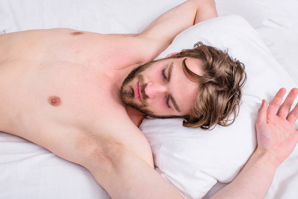 Man sleepy drowsy bearded face having rest. Pleasant awakening concept. Guy sleepy morning nap. Man unshaven handsome guy naked torso relaxing bed top view. Guy sexy macho lay white bedclothes - Photo, Image
