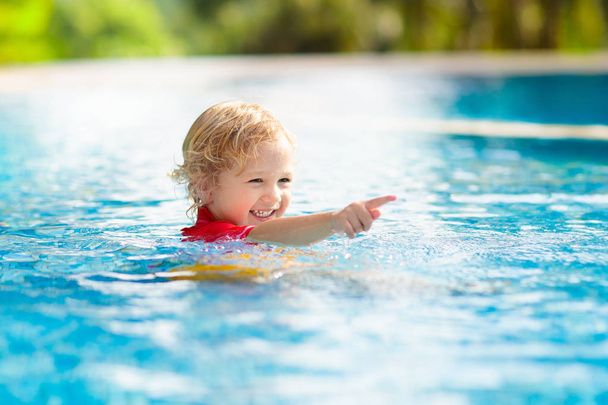 子供たちはプールで遊んでいる。子供たちと夏休み。熱帯の島のリゾートでエキゾチックな休日の間に水に飛び込む小さな男の子。子供たちは泳ぐ。未就学児のためのアクティブな屋外スポーツ. - 写真・画像