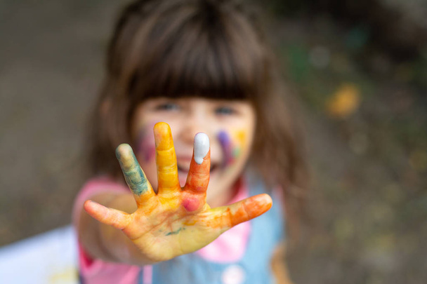 Το παιδί δείχνει ζωγραφισμένα χέρια. Πορτρέτο του αξιολάτρευτο κοριτσάκι χαμογελώντας ευτυχώς απολαμβάνοντας την τέχνη και η τέχνη. - Φωτογραφία, εικόνα