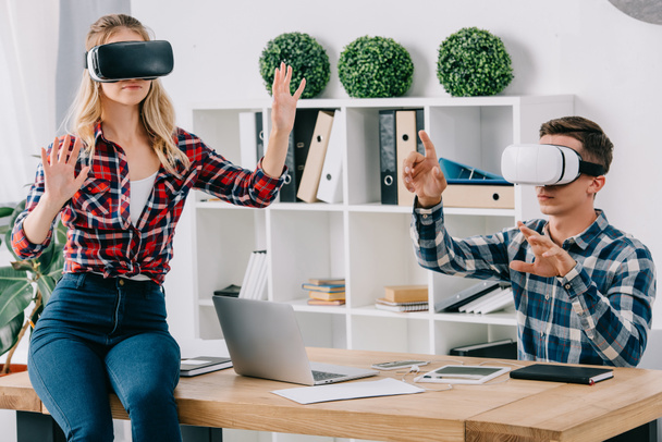 young businesspeople in virtual reality headsets gesturing at workplace in office - Fotografie, Obrázek