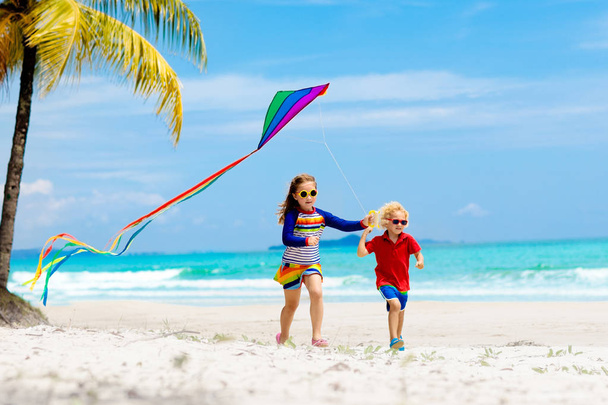 Tropikal plaj renkli uçurtma ile çalışan çocuk. Çocuk uçan gökkuşağı uçurtma. Oyuncak uçak ile deniz kıyısında oynayan küçük bir kız. Egzotik ada aile yaz tatili. Su ve kum eğlenceli çocuklar için.  - Fotoğraf, Görsel