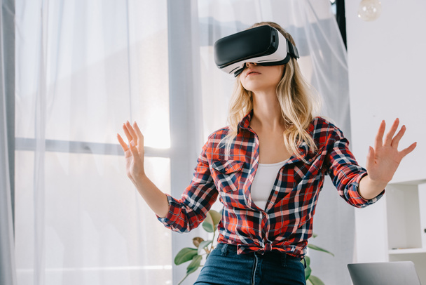 young woman in virtual reality headset gesturing in room - Foto, Imagen