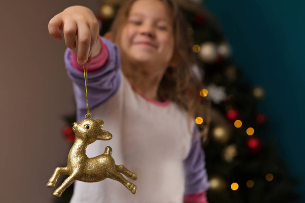 Happy Young Girl Smiling Holding Gold Reindeer Ornament - Фото, изображение