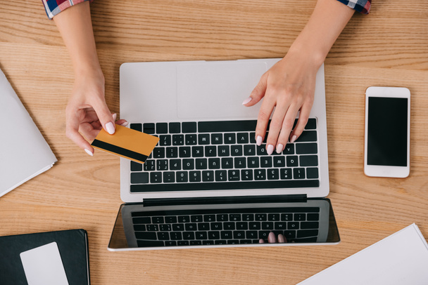 vista parcial de la mujer con tarjeta de crédito haciendo compra en línea en la mesa de madera
 - Foto, imagen