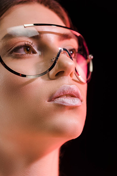 portrait of beautiful woman in fashionable eyeglasses looking away isolated on black - 写真・画像