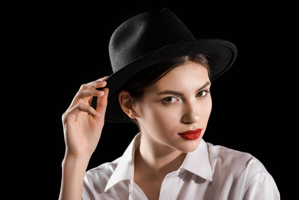 Portret van stijlvolle vrouw in zwarte hoed en witte overhemd poseren geïsoleerd op zwart - Foto, afbeelding