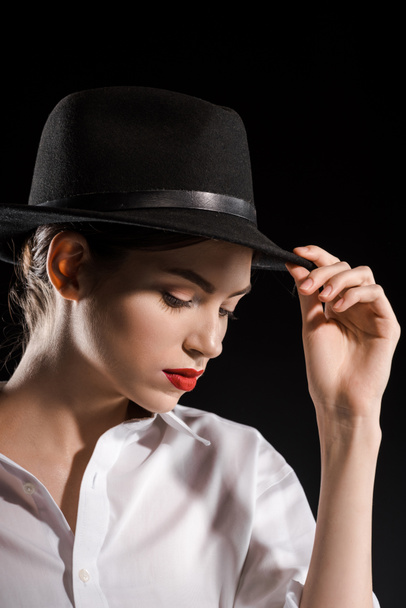portrait of beautiful woman in white shirt and black hat posing isolated on black - 写真・画像