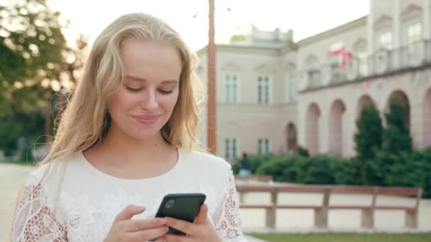 Mladá blondýnka dáma chůzi a používání telefonu ve městě - Záběry, video