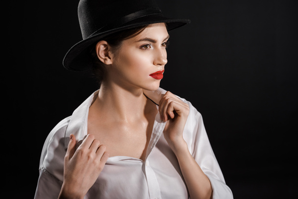 portrait of beautiful pensive woman in white shirt and black hat posing isolated on black - Foto, Imagem