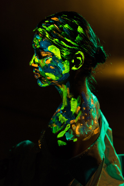 side view of woman painted with colorful ultraviolet paints on black backdrop - Fotoğraf, Görsel