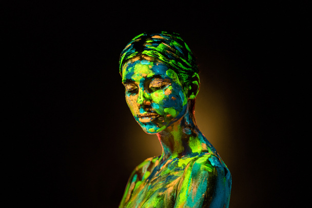 Porträt einer schönen Frau mit bunten ultravioletten Farben auf dem Körper auf schwarzem Hintergrund - Foto, Bild
