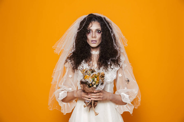 死んだ花嫁のウェディング ドレスと黄色の背景に分離カメラに笑顔怖いメイクを身に着けているハロウィーンのゾンビのイメージ - 写真・画像