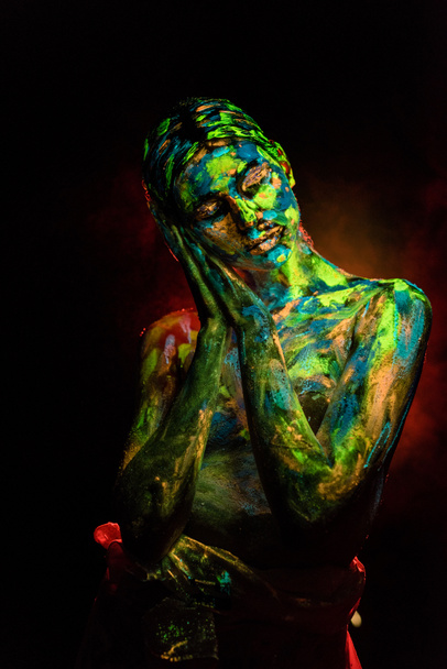 portrait of beautiful woman with colorful ultraviolet paints on body on black backdrop - Фото, изображение