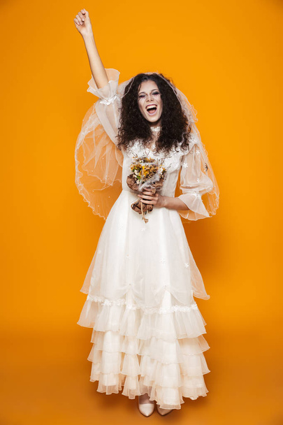 Happy bride zombie in wedding dress and veil screaming and laughing isolated over orange - Foto, imagen
