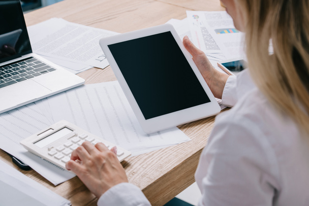 visión parcial de la mujer de negocios con tableta haciendo cálculos en el lugar de trabajo con papeles
 - Foto, Imagen