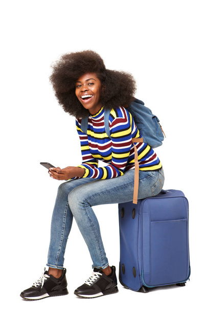 Portrait of young african american female traveler sitting on suitcase with mobile phone - Valokuva, kuva