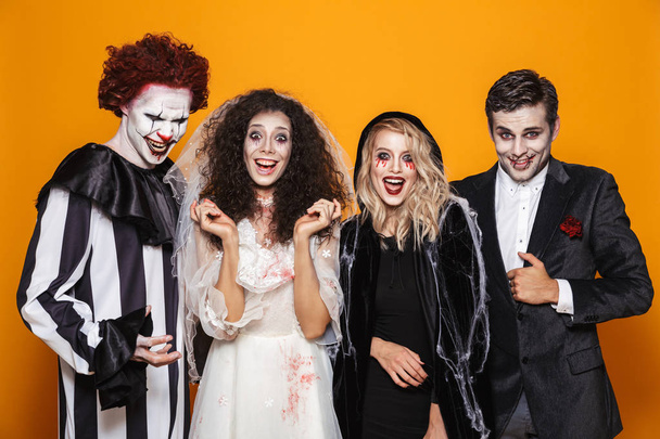 Grupo de amigos alegres vestidos con trajes de miedo celebrando Halloween aislados sobre fondo amarillo
 - Foto, Imagen