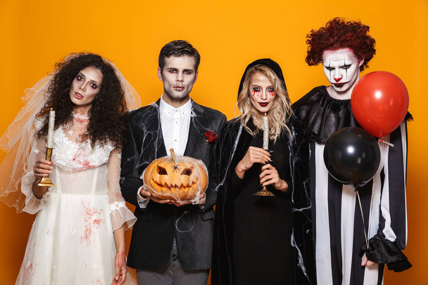 Group of friends dressed in scary costumes celebrating Halloween isolated over yellow background - Φωτογραφία, εικόνα