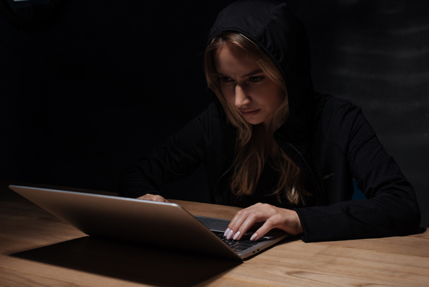 portrait of woman in black hoodie using laptop, cyber security concept - 写真・画像
