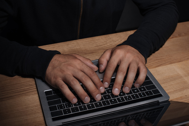 cropped shot of hacker using laptop at wooden tabletop, cuber security concept - Fotó, kép