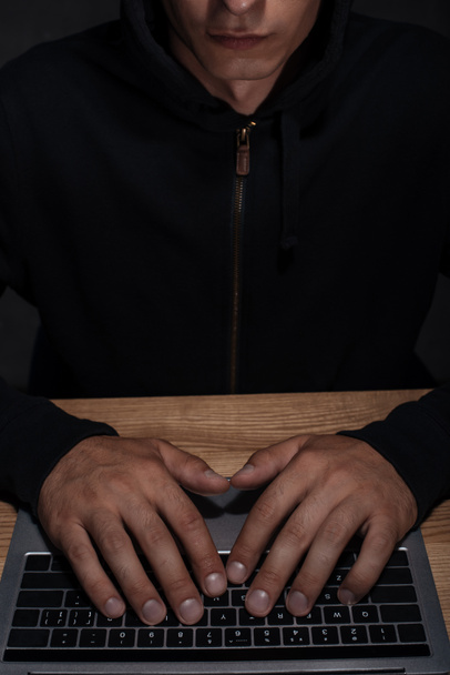 partial view of hacker in black hoodie using laptop, cuber security concept - Fotó, kép