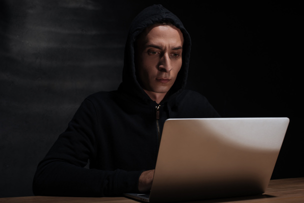 portrait of hacker in black hoodie using laptop, cuber security concept - Foto, imagen