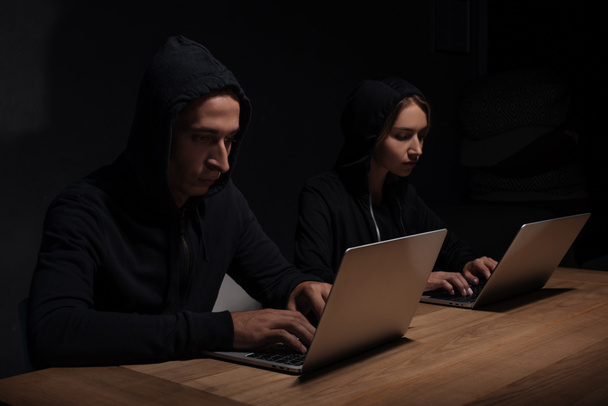 hackers enfocados en sudaderas con capucha negra usando computadoras portátiles en habitación oscura, concepto de seguridad cibernética
 - Foto, Imagen
