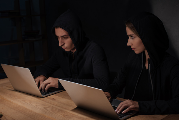 hackers en sudaderas con capucha negra usando computadoras portátiles en la mesa de madera, concepto de seguridad cibernética
 - Foto, Imagen