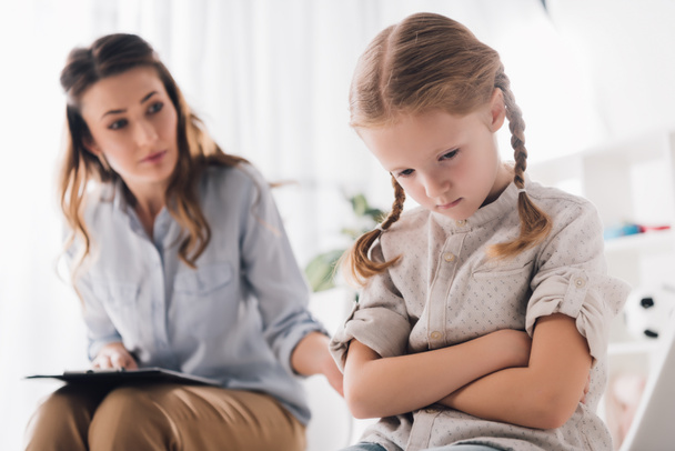 adult psychologist talking to depressed child with crossed arms - Foto, Imagem