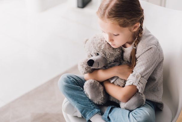 high angle view of depressed little child embracing her teddy bear - Foto, Imagen