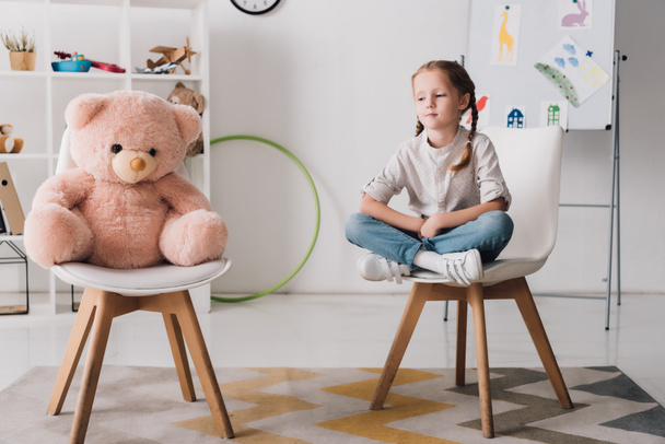 lonely little child sitting on chair near pink teddy bear - Photo, Image