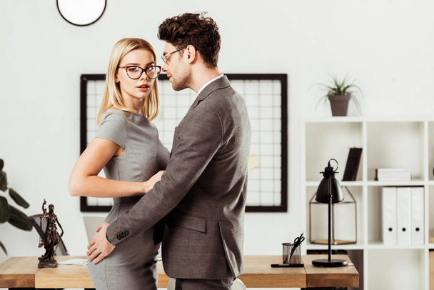 young lawyers hugging each other while standing in office, flirt and office romance concept - Fotografie, Obrázek