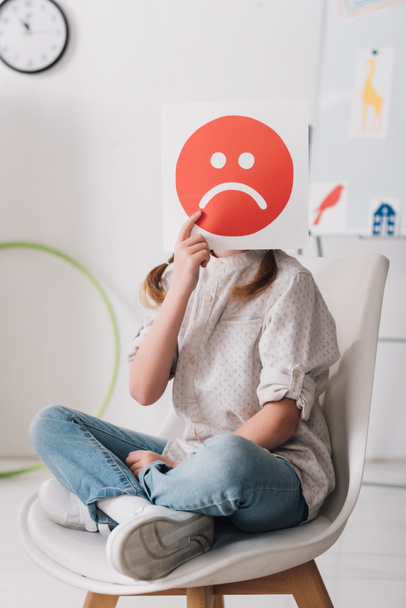 little child sitting on chair and covering face with sad face symbol - Photo, Image