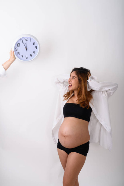 Portrait of beautiful young pregnant Asian woman looking clock - 写真・画像