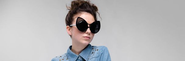 Young brunette girl in black glasses. Cat glasses. The hair is gathered in a bun. The girl folded her arms. The girl is laughing. - Foto, Imagen