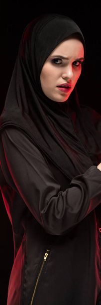 Portrait de belle jeune femme musulmane effrayée et sérieuse portant le hijab noir appelant à l'aide sur fond noir
 - Photo, image