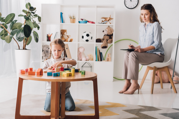 little child playing with blocks while psychologist sitting blurred on background - Photo, Image