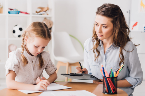 adult psychologist sitting near child drawing with color pencils - Photo, Image