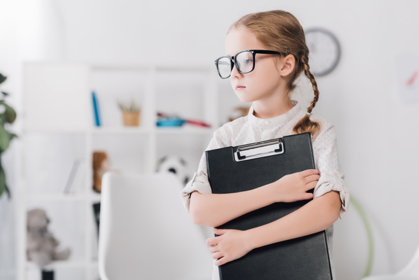 serious little child in eyeglasses holding clipboard and looking away - Photo, image
