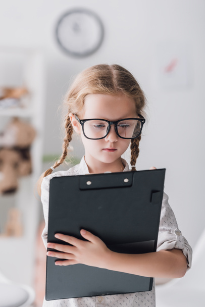 close-up portrait of little child in eyeglasses writing in clipboard - 写真・画像