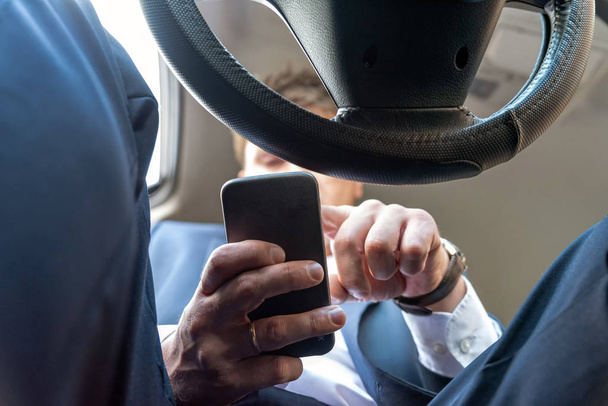 Businessman working on tablet and smartphone inside car on bright day - Фото, изображение